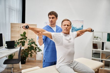 good looking mature patient using dumbbells with help of his dedicated doctor, rehabilitation