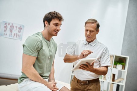 good looking mature doctor checking up knees of his patient in hospital, rehabilitation concept