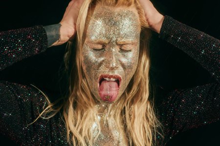 Photo for Portrait of provocative woman with glitter on face and body rolling eyes on black background - Royalty Free Image