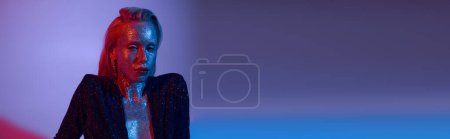 Banner der verführerischen Frau mit Glitzerbezug posiert in glänzendem Outfit unter farbigen Lichtern im Studio