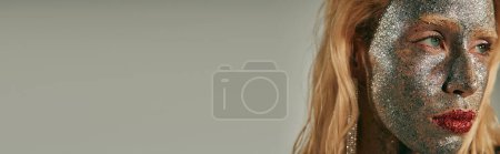 Téléchargez les photos : Bannière de gros plan, jeune femme avec des yeux verts et des paillettes sur tout le corps et le visage sur fond gris - en image libre de droit