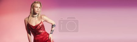 beautiful woman in stylish red dress on pink backdrop with hand on hip looking away, banner