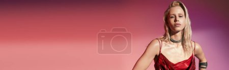 belle femme blonde en robe rouge chic posant sur fond rose et regardant la caméra, bannière