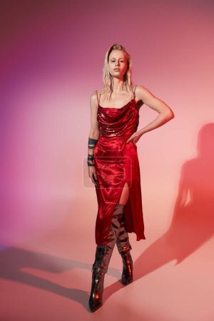 mujer sexy de buen aspecto en vestido elegante rojo posando con su mano en la cadera y mirando a la cámara