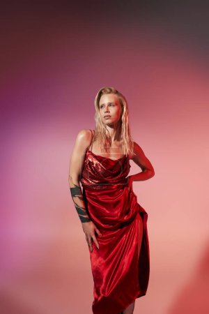 good looking young woman with tattoo in red dress posing in motion with hand on hip on pink backdrop