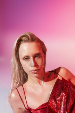 portrait of beautiful woman with green eyes in red dress on pink backdrop looking at camera
