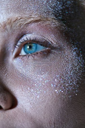 Foto de Primer plano de la joven con el ojo azul y destellos brillantes en su cara mirando hacia otro lado, resaltador - Imagen libre de derechos