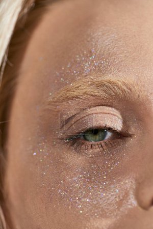 close up of young woman with green eye and shiny glitter on her face looking at camera, highlighter