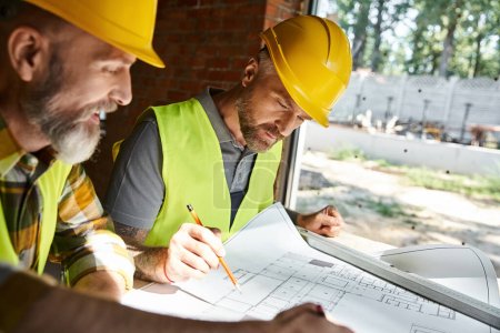 Photo for Two handsome builders in safety helmets and vests working with blueprint before construction - Royalty Free Image