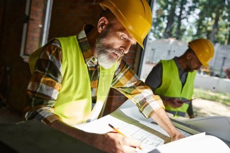Photo for Handsome worker looking at blueprint with his colleague working on backdrop, cottage builders - Royalty Free Image