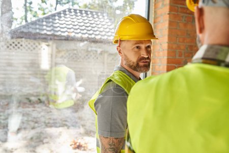 Téléchargez les photos : Se concentrer sur travailleur barbu casque de sécurité parler à son collègue sur le chantier, constructeurs - en image libre de droit