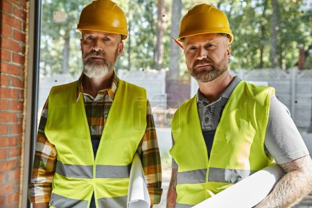 Photo for Good looking dedicated builders in safety vests and helmets looking at camera on construction site - Royalty Free Image