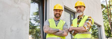 jolly workers in safety vests with arms crossed looking at camera, cottage builders, banner