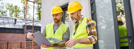 Photo for Handsome men in safety vests and helmets working with laptop on construction site, builders, banner - Royalty Free Image