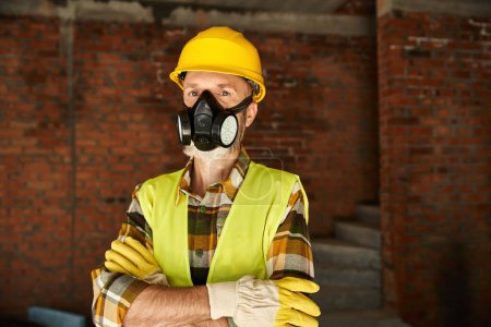 handsome cottage builder with dust mask in safety helmet with arms crossed looking at camera