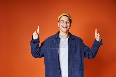 Photo for Attractive smiling man in his 20s pointing with fingers up against terracotta background - Royalty Free Image
