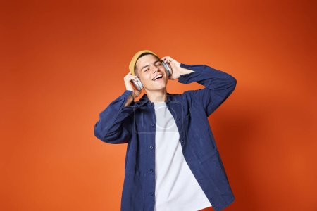 attraktiver junger Kerl hört gerne Musik mit Kopfhörern auf Terrakottahintergrund