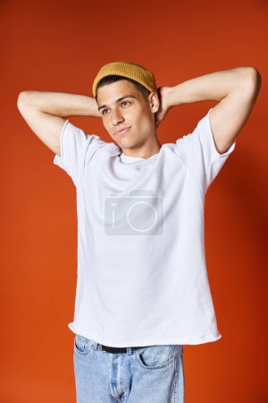 encantador joven en camiseta blanca y sombrero amarillo de pie poniendo las manos detrás de la espalda