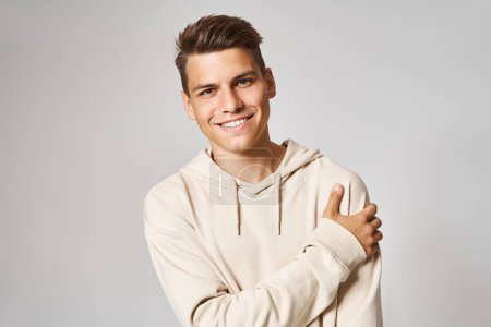 portrait of young man in white hoodie holding to shoulder against light background