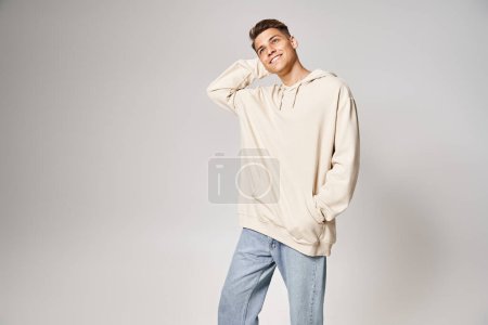 attractive man in white hoodie putting hand behind head and looking to up against light background