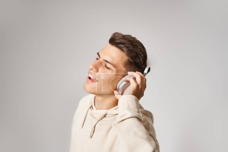 profile of cheerful man in white hoodie listening to music with closed eyes on light background