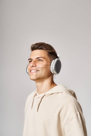 Téléchargez les photos : Jeune homme souriant avec les cheveux bruns dans les écouteurs regardant vers le haut sur fond clair - en image libre de droit