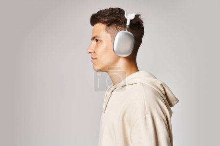 Téléchargez les photos : Profil de jeune homme confiant avec les cheveux bruns dans les écouteurs sur fond clair - en image libre de droit