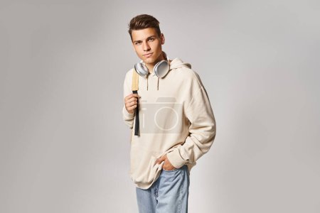cheerful student in headphones and casual outfit with backpack posing against grey background