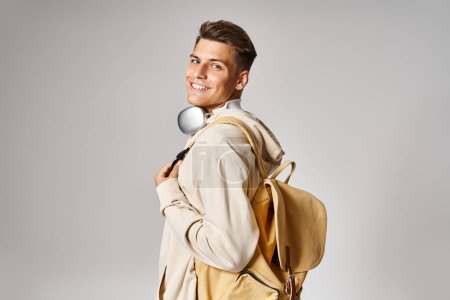 smiling student in headphones and casual outfit with backpack looking from behind back