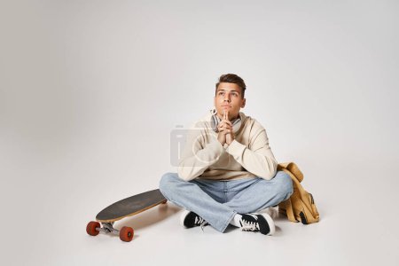 Photo for Hopeful student in headphones sitting with backpack and skateboard and folding hands together - Royalty Free Image