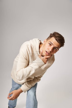 charismatic young guy leaning to forward and touching to jawline against grey background