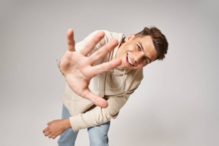 Foto de Atractivo hombre inclinado hacia adelante y extendiendo su mano a la cámara sobre fondo gris - Imagen libre de derechos