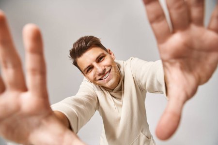 Foto de Hombre alegre con el pelo castaño y los ojos grises extendiendo sus manos a la cámara sobre fondo claro - Imagen libre de derechos