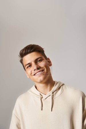 portrait of smiling young man with brown hair and grey eyes leaning head against light background