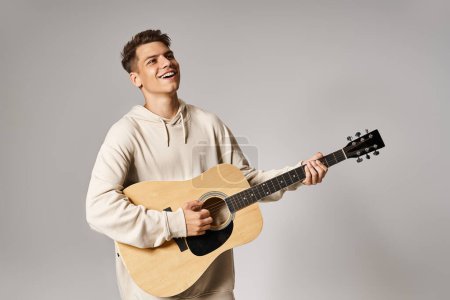 Foto de Atractivo hombre de 20 años con cabello castaño tocando la guitarra sobre fondo claro - Imagen libre de derechos