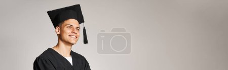 Horizontale Aufnahme einer attraktiven Studentin in Diplomatenkleid und Mütze, die lächelnd nach vorne blickt