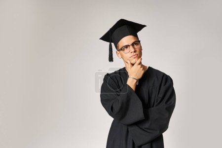 tipo reflexivo en traje de graduado y gafas de visión tocando la mano a la mandíbula sobre fondo gris