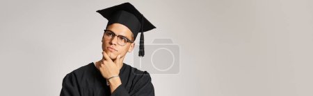 banner of thoughtful man in graduate outfit and vision glasses touching hand to jawline