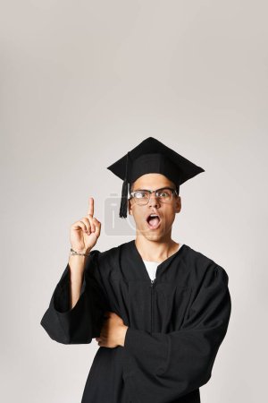 attractive young student in graduate outfit and vision glasses come up to idea on grey background