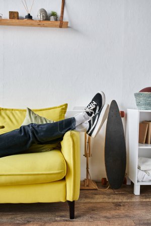 cropped shot of man legs in black sneakers lying to cross on yellow couch in living room