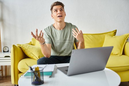 hombre guapo en el sofá amarillo con el ordenador portátil en la mesa de café hablando admiración a la reunión en línea
