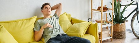Photo for Banner of tired young man putting hand behind head and leaning on yellow couch with glasses - Royalty Free Image