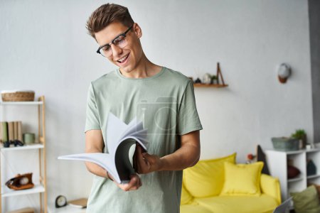 glücklicher und charmanter Kerl mit braunen Haaren und Brille im Wohnzimmer beim Lesen von Notizen