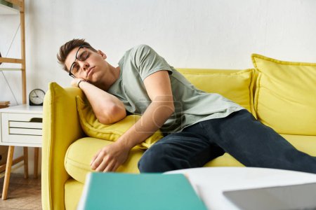 Téléchargez les photos : Jeune étudiant fatigué aux cheveux bruns et lunettes de vision dormant sur un canapé jaune dans le salon - en image libre de droit