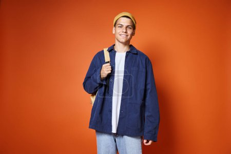 charming young man in yellow hat with backpack smiling against terracotta background