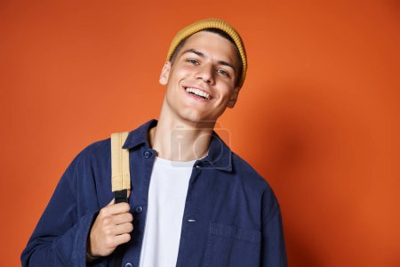 Foto de Retrato de chico guapo sonriente en sombrero amarillo con mochila contra fondo de terracota - Imagen libre de derechos