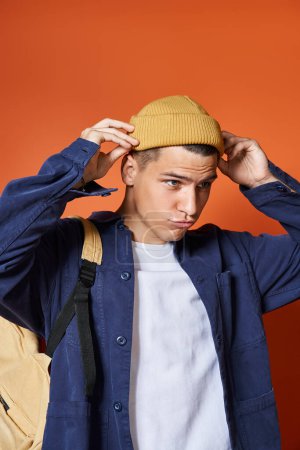Photo for Attractive young man with backpack adjusting his yellow hat on terracotta background - Royalty Free Image