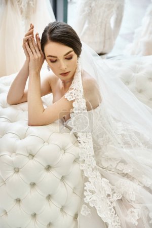 Eine junge brünette Braut im Brautkleid liegt anmutig auf einem Plüschsofa in einem luxuriösen Brautsalon.