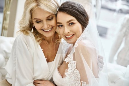 Photo for A young brunette bride in a wedding dress and her middle-aged blonde mother stand side by side in a bridal salon. - Royalty Free Image