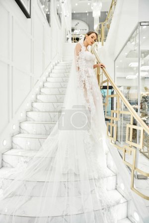 Une jeune mariée brune dans une robe de mariée se tient sur un escalier dans un salon de mariée.